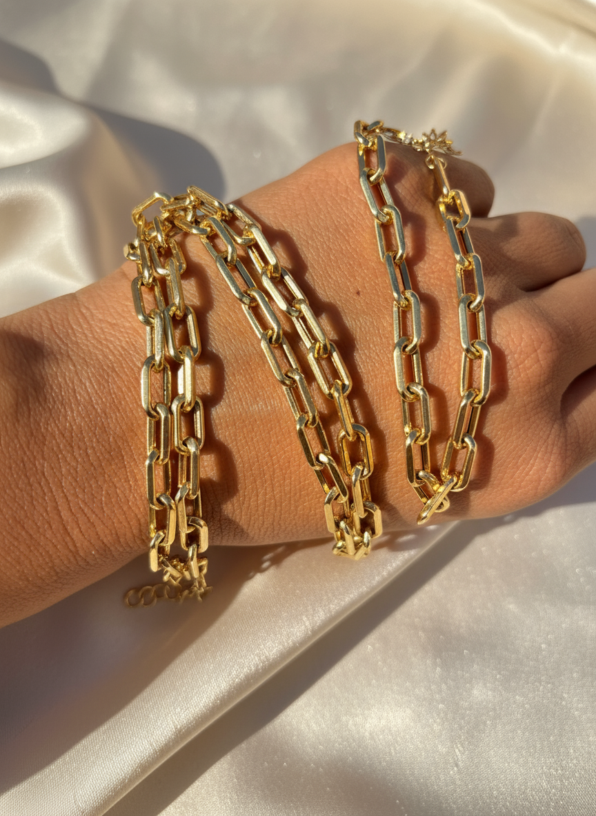 Gold paperclip bracelets on hand with ivory background