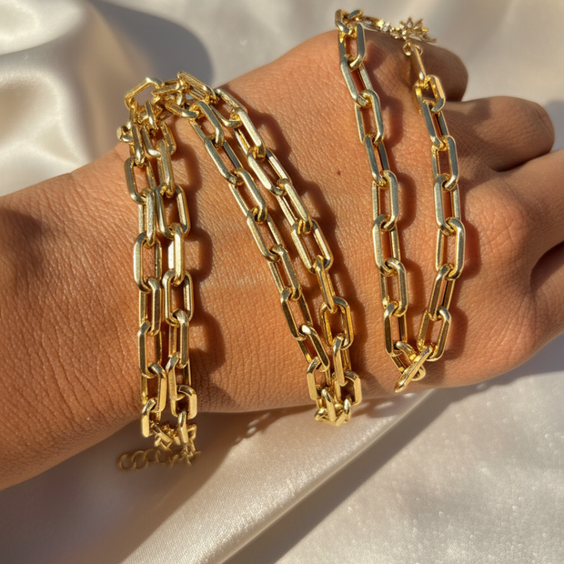 Gold paperclip bracelets on hand with ivory background