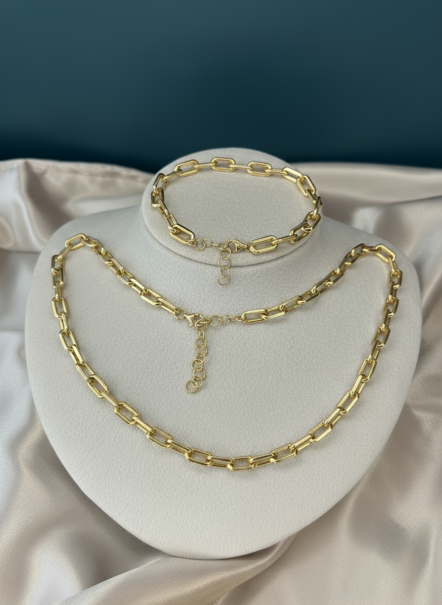 Gold paperclip jewelry set on ivory display with teal background